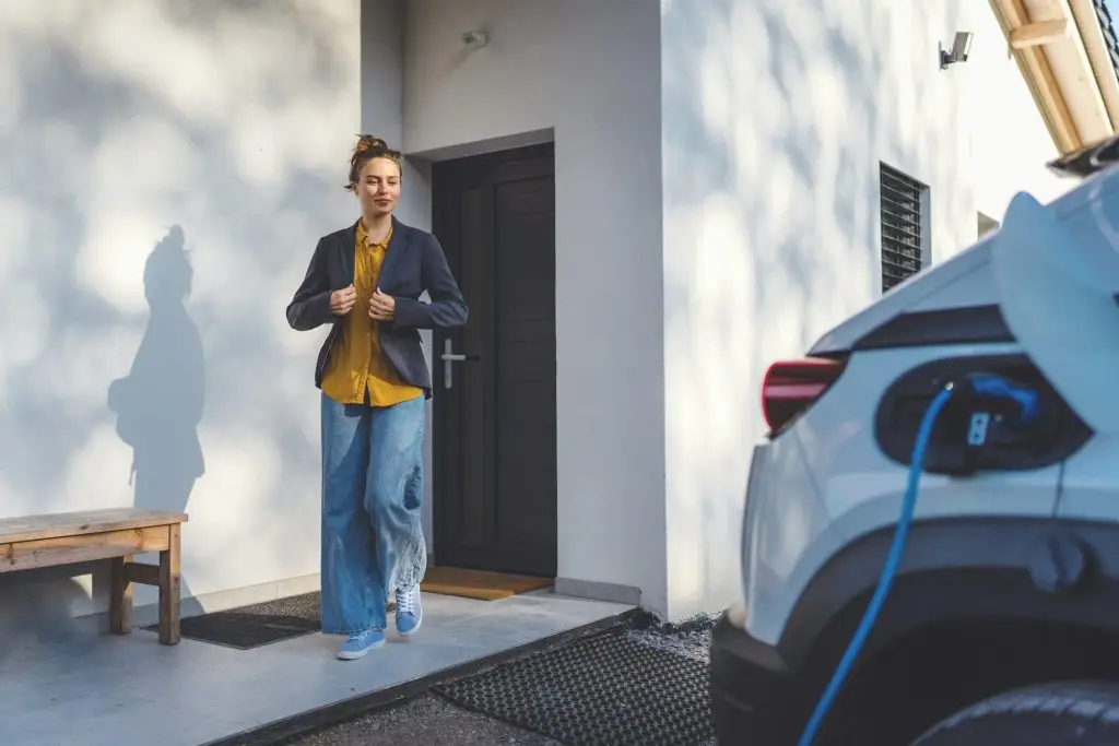 Young woman preparing to work while her electric car charging in home, sustainable and economic